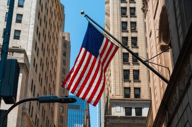 New York, Manhattan 'daki binaya karşı Amerikan bayrağı. Wall Street ve ABD bayrakları farklı binalar arasında