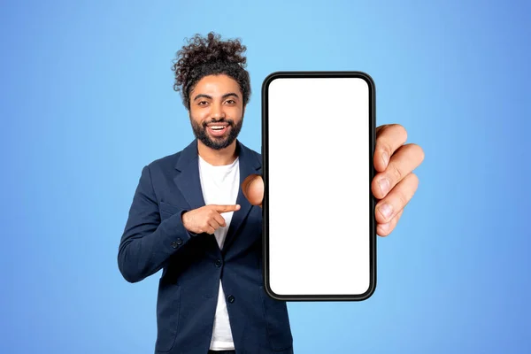 幸せな中東のビジネスマンは 青い背景にカメラを見て笑顔の肖像画 モックアップの空白の画面でスマートフォンを指している オンラインショッピングの概念 — ストック写真