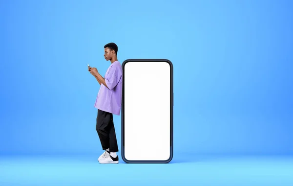 携帯電話を持つアフリカ系アメリカ人の男性は デバイスの近くの完全な長さは コピースペースディスプレイ ライトブルーの背景をモック ソーシャルメディアとコミュニケーションの概念 — ストック写真