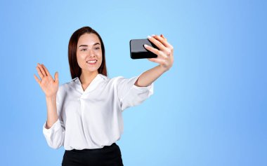 Akıllı telefonlu gülümseyen iş kadını, video görüşmesi yapıyor ve mavi arka planda el sallıyor. Online ağ kavramı. Boşluğu kopyala