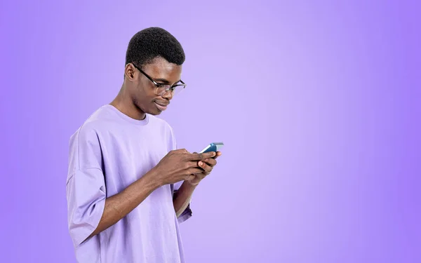 拿着智能手机工作的美国黑人 网上浏览 发短信紫色背景 网络和社交媒体的概念 复制空间 — 图库照片