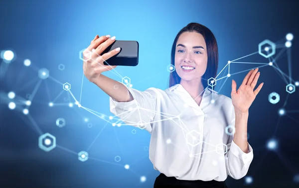 Young businesswoman making a video call, waving hand and holding smartphone. Network hologram double exposure and circuit of connection in metaverse. Concept of social media