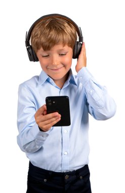 Kulaklıklı gülümseyen çocuk akıllı telefona bakıyor, beyaz arka planda izole edilmiş. Video çağrısı, çevrimiçi eğitim ve mobil uygulama kavramı