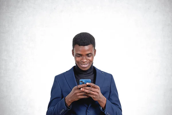 コンクリートの壁の背景に立ってスマートフォンを使用して陽気な若いアフリカ系アメリカ人ビジネスマンの肖像画 コミュニケーションの概念 — ストック写真