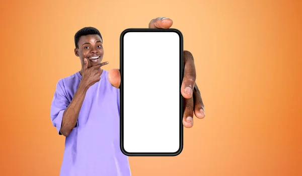 아프리카 청년은 행복하게 웃으면서 커다란 스마트폰을 손가락으로 가리키며 복사된 주황색 — 스톡 사진