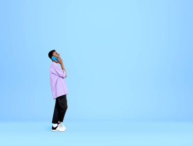 Sıradan kıyafetler giyen Afro-Amerikalı yakışıklı işadamı arka plandaki boş mavi duvarın yanında akıllı telefondan konuşuyor. Çalışma süreci kavramı, mesafe çalışması, önemli konferans çağrısı