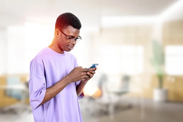黒人アメリカ人の男性はスマートフォン 肖像画で入力笑みを浮かべて オンラインで閲覧し ぼやけたオフィスルームの背景にチャット 距離作品とソーシャルメディアの概念 — ストック写真