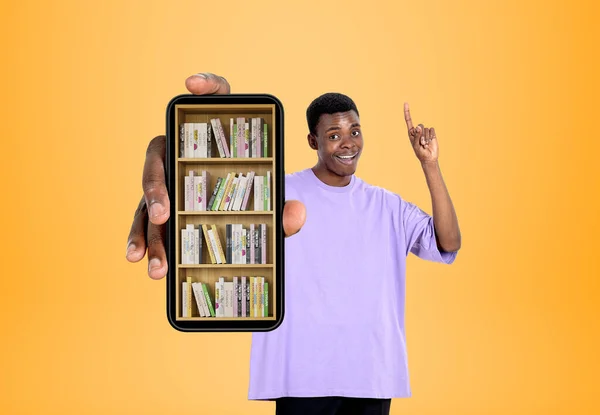 笑顔の空白の男の指をポイントし 黄色の背景にデジタルライブラリを手にスマートフォン 棚の上に電子書籍とスマートフォン Eラーニングの概念 — ストック写真