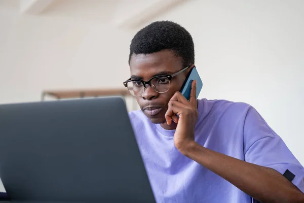 Концентрированный Африканский Бизнесмен Звонит Телефону Смотрит Экран Ноутбука Вдумчивым Взглядом — стоковое фото