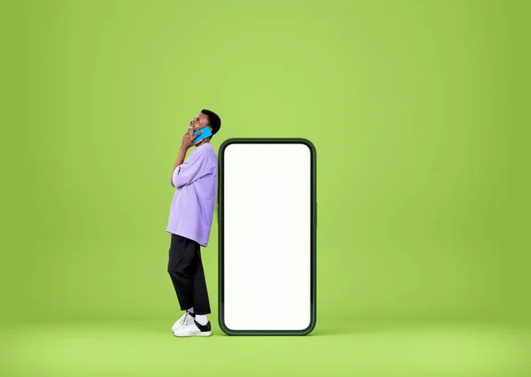 黒の若い男がスマートフォンの近くに立って 話して 笑っている 緑色の背景にコピースペースの画面をモックアップします モバイルアプリとネットワークの概念 — ストック写真