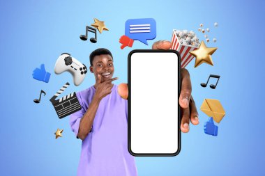 Gülümseyen Afrikalı adam telefon ekranını işaret ediyor, farklı dijital eğlence simgeleri yüzüyor. Mobil uygulama, çevrimiçi alışveriş ve oyun kavramı