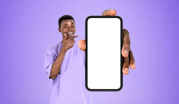 黒の若い男 指のコピースペース画面 紫色の背景をモックアップ大規模なスマートフォンを指して笑顔 ウェブサイトとオンラインショッピングの概念 — ストック写真