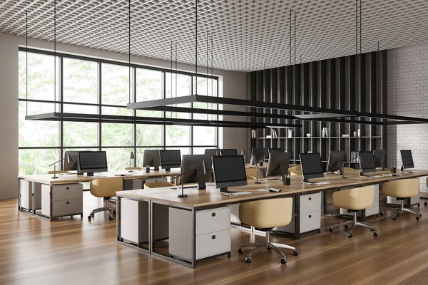 stock image Stylish office interior with armchairs and pc computer on shared desk in row, side view hardwood floor. Coworking corner with shelf and panoramic window. 3D rendering