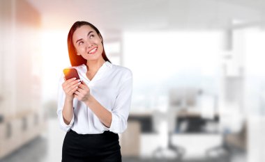 Gülümseyen iş kadını telefonu elinde kullanıyor, internette geziniyor, düşünüyor ve hayal kuruyor. Bulanık arka planda Ceo ofis odası. İş ağı ve sosyal medya kavramı