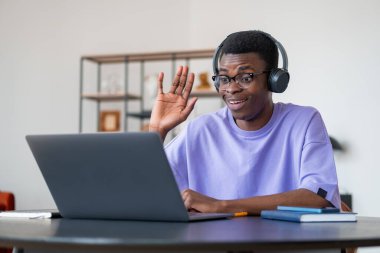 Kulaklıkla gülümseyen Afrikalı işadamı, el sallıyor ve dizüstü bilgisayarına bakıyor, online video konferansı. Web iletişimi ve mesafe çalışması. Müzakere kavramı
