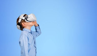 VR gözlüklü çocuk portresi profili, boş fotokopi alanı mavi arkaplanına bakıyor. Sanal gerçeklik kavramı, gelecekteki teknoloji ve metaevrendeki eğlence