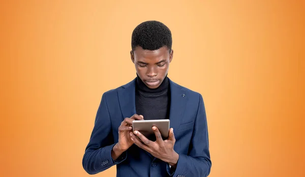 Serious black businessman working in tablet, concentrated portrait. Business network and social media, copy space empty orange background. Concept of online communication