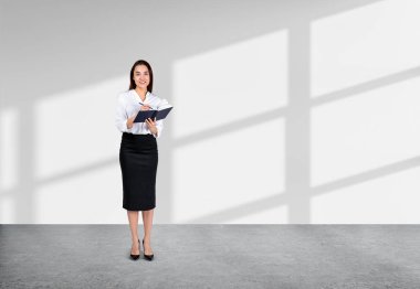 Gülümseyen iş kadını not defterine not alıyor. Gri beton zeminde tam boy ve beyaz boş arkaplan. Fikir ve başlangıç kavramı. Boşluğu kopyala