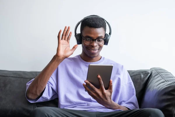 Χαμογελώντας Νεαρός Αφρικανός Επιχειρηματίας Ακουστικά Κουνώντας Χέρι Και Κοιτάζοντας Tablet — Φωτογραφία Αρχείου