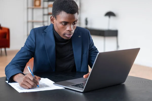Африканский Бизнесмен Смотрит Экран Ноутбука Записывает Бумагу Офисная Комната Отделкой — стоковое фото