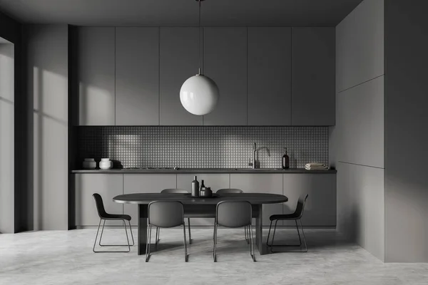 stock image Dark kitchen interior with dining table and chairs, grey concrete floor. Kitchenware and hidden cabinets, minimalist shelves and window. 3D rendering