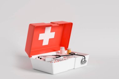 Kırmızı ilk yardım çantası, haplar ve steteskop açık gri arka planda yan görüş. Acil durum ve doktor kavramı. 3B görüntüleme