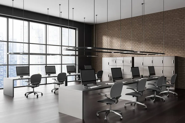 Corner of modern open space office with gray and brown brick walls, dark wooden floor, row of computer tables with gray chairs and beige cabinets. Panoramic window with cityscape. 3d rendering