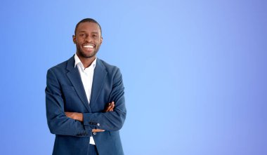 Mavi arka planda kollarını kavuşturmuş, gülümseyen Afro-Amerikan iş adamının portresi. Model