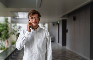 Mutlu iş adamı telefonda arıyor, ofis koridorunun arka planında duran kameraya bakıyor. İş ağı, bağlantı ve çevrimiçi iletişim kavramı