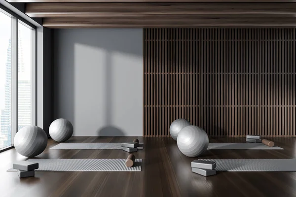 Interior of modern yoga studio with gray and dark wooden walls, dark wooden floor, yoga mats and gray fitballs. 3d rendering