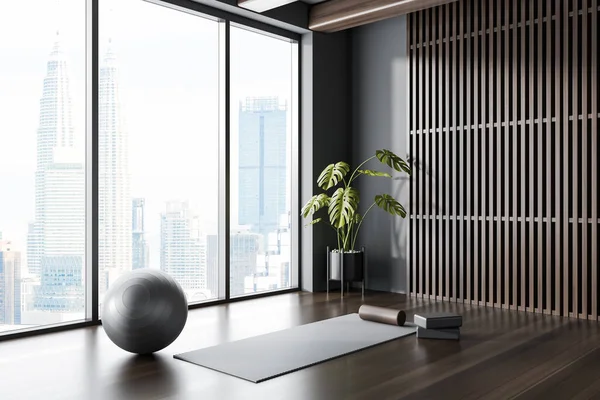 Corner of panoramic yoga studio with gray and dark wooden walls, dark wooden floor, yoga mat and gray fitball. 3d rendering