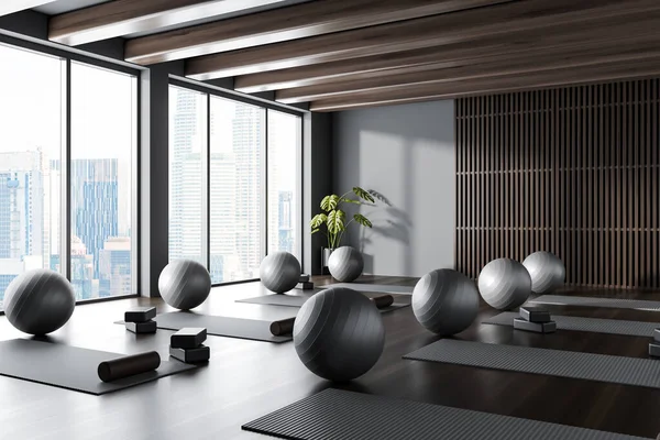 Corner of modern yoga studio with gray and dark wooden walls, dark wooden floor, yoga mats and gray fitballs. 3d rendering