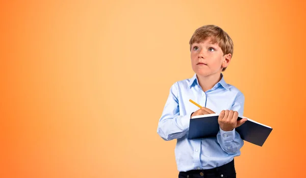 Portrait Serious Little Boy Writing Black Notebook Pen Orange Background — Stock Photo, Image