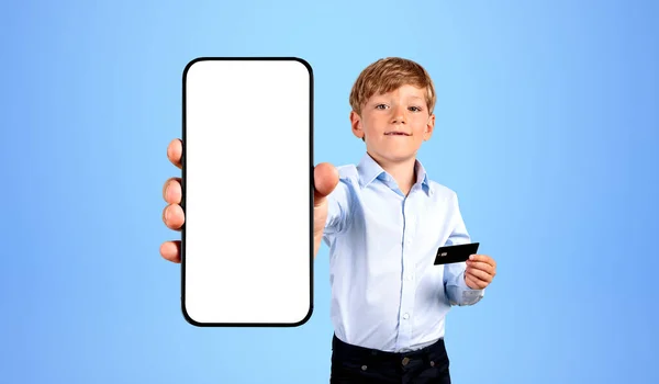 Child holding smartphone with mock up empty display, holding a credit card in hand on blue background. Concept of online payment, transaction and shopping