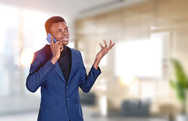正式なスーツを着たハンサムなアフリカ系アメリカ人ビジネスマンが背景にオフィスの職場でスマートフォンで話して立っています 取引の概念 モバイル通信 会議コール — ストック写真