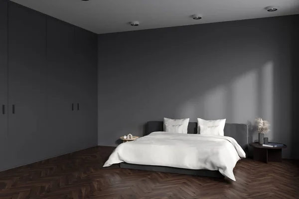 Corner view on dark bedroom interior with empty grey wall, bed, coffee table, pillows, lamp, houseplant, oak wooden hardwood floor. Concept of minimalist design. Space for creative idea. 3d rendering