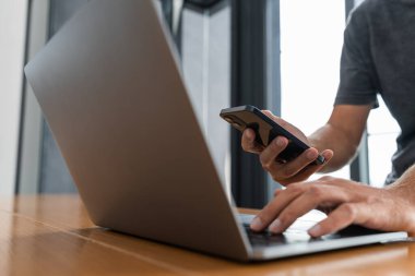 Ofiste dizüstü bilgisayar ve akıllı telefon kullanan tanınmayan iş adamının elleri. Modern teknoloji ve iletişim kavramı