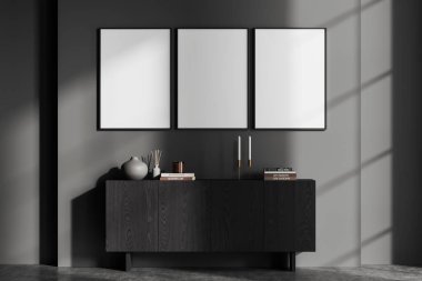 Ahşap şifoniyer ve sanat dekorasyonu olan karanlık bir oturma odası. Sıcak İskandinav tasarımı ve gri beton zemin. Sıraya dizilmiş üç tane tuval posteri. 3B görüntüleme