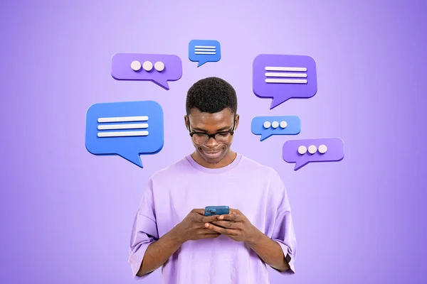 African smiling man typing in phone, text message bubbles icons on purple background. Concept of social media, online communication and mobile app