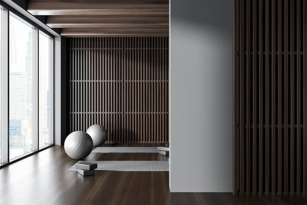 Interior of modern yoga studio with gray and dark wooden walls, dark wooden floor, yoga mats and gray fitballs. Blank wall on the right. 3d rendering