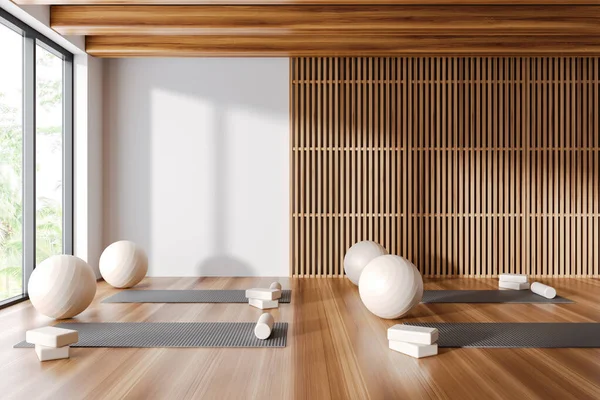 Interior of stylish yoga studio with white and wooden walls, wooden floor, yoga mats and white fitballs. 3d rendering