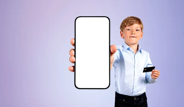 男孩展示了一个巨大的智能手机与模拟空显示 手持信用卡紫色背景 网上购物 付款及流动应用的概念 — 图库照片