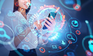 Akıllı telefon kullanan gülümseyen bir iş kadını. Işıldayan simgeli dünya hologramı. Tarayıcı ve bağlantı kavramı