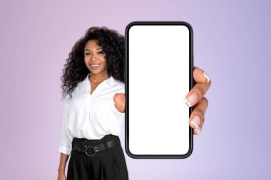 Resmi kıyafet giyen Afro-Amerikalı iş kadını arka plandaki mor duvarın önünde duran sahte ekranlı akıllı telefonu tutuyor. Mobil uygulama ve sosyal medya sunumu