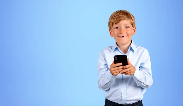 青い背景の上にスマートフォンを使用して青いシャツの笑顔の男の子の肖像画 ソーシャルメディアとコミュニケーションの概念 スペースのコピー — ストック写真