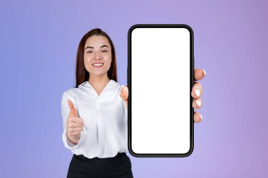 İş kadını başparmağıyla gülümsüyor, akıllı telefonu tutan kameraya bakıyor, büyük bir kopya uzay ekranı, gradyan mor arka plan. Takip ve abone kavramı