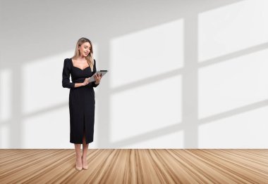 Ofis zemininde siyah elbiseli genç bir iş kadını, tablette internette geziniyor. Bağlantı ve ağ kavramı. Boşluğu kopyala