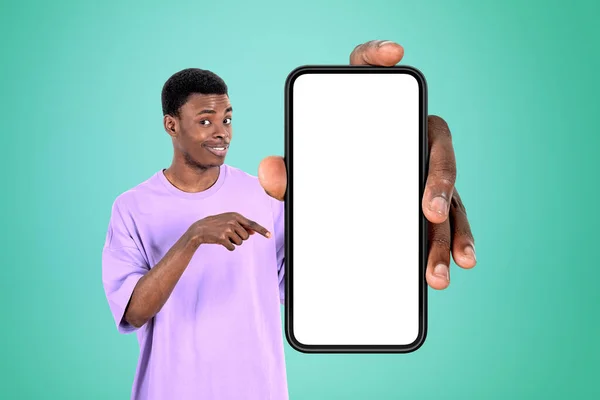黒の若い男 指のコピースペース画面 緑の背景をモックアップ大規模なスマートフォンを指して笑顔 ウェブサイトやモバイルアプリの概念 — ストック写真