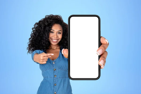 黒人女性の笑顔 指の大きなスマートフォンのモックアップをコピースペースディスプレイ 青の背景を指している ソーシャルメディアとウェブサイトの概念 — ストック写真