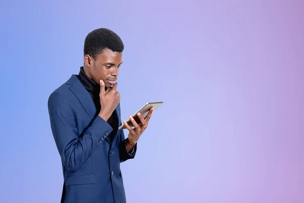 正式なスーツを着たハンサムなアフリカ系アメリカ人実業家が背景に空の紫色の壁の近くのタブレットデバイスで見て立っている 現代のガジェットの概念 モバイル通信 時間管理 — ストック写真